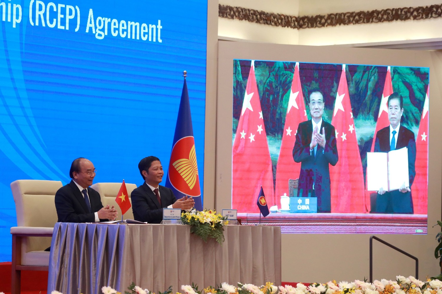 Vietnamese Prime Minister Nguyen Xuan Phuc, left, and Minister of Trade Tran Tuan Anh, right, applaud next to a screen showing Chinese Premier Li Keqiang and Minister of Commerce Zhong Shan holding up signed RCEP agreement, in Hanoi, Veitnam. China and 14 other countries have agreed to set up the world's largest trading bloc, encompassing nearly a third of all economic activity, in a deal many in Asia are hoping will help hasten a recovery from the shocks of the pandemic. (AP Photo/Hau Dinh)